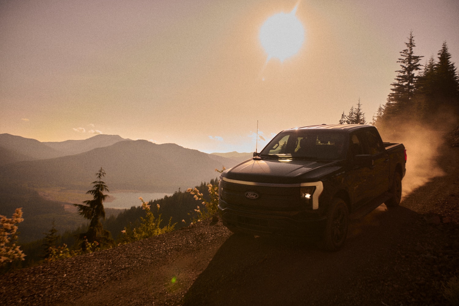 A black F-150 Lightning parked on a mountain ridge, seen from the back, at dusk with a mountain skyline in the background.